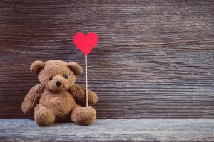 Teddy bear with heart sitting on old wood background.